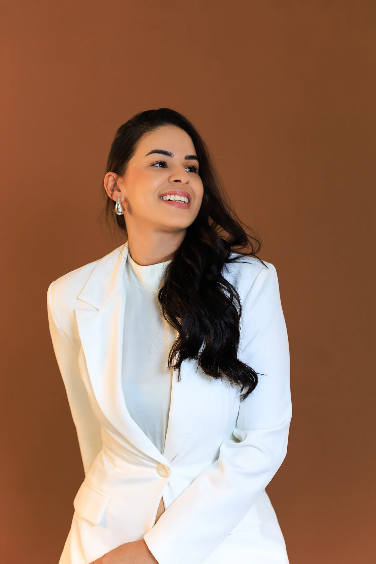 Mislley Santos de blazer branco, sorrindo, em frente a um fundo quente.